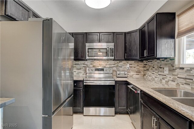 kitchen with light tile patterned flooring, dark brown cabinetry, stainless steel appliances, light stone countertops, and decorative backsplash