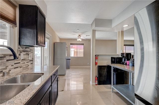 kitchen with sink, light tile patterned floors, stainless steel refrigerator, light stone countertops, and backsplash