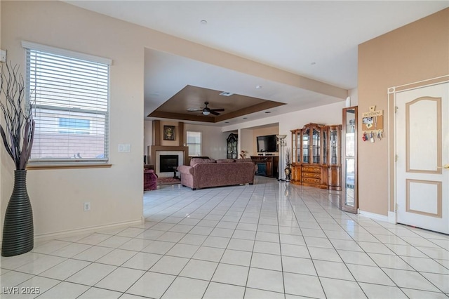 unfurnished living room featuring light tile patterned flooring, ceiling fan, and a raised ceiling