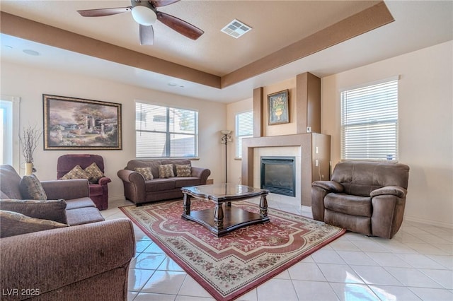 living room featuring a tiled fireplace, ceiling fan, a raised ceiling, and light tile patterned floors