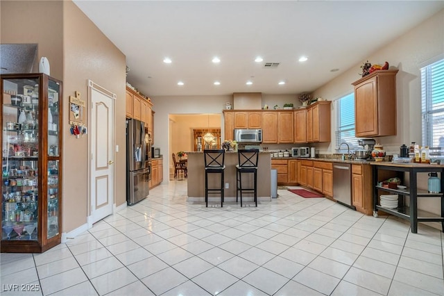 kitchen with a kitchen bar, a kitchen island, light tile patterned flooring, and appliances with stainless steel finishes