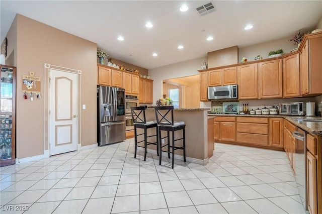 kitchen with appliances with stainless steel finishes, a breakfast bar area, dark stone counters, a center island, and light tile patterned floors