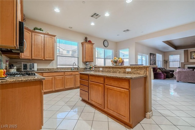 kitchen featuring a kitchen island, stainless steel gas stovetop, sink, light tile patterned floors, and light stone counters