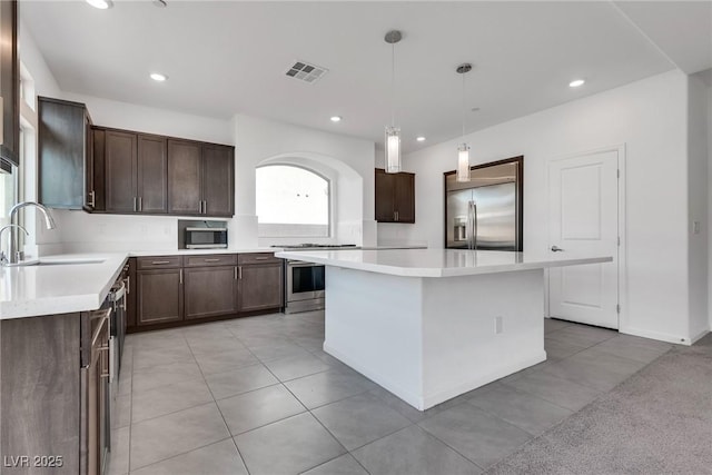 kitchen with a kitchen island, appliances with stainless steel finishes, decorative light fixtures, sink, and dark brown cabinets