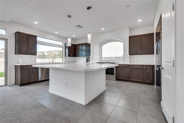 kitchen with dark brown cabinets, hanging light fixtures, light tile patterned floors, stainless steel range, and a kitchen island