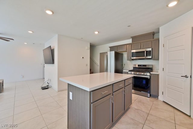 kitchen featuring light tile patterned floors, ceiling fan, gray cabinetry, stainless steel appliances, and a kitchen island