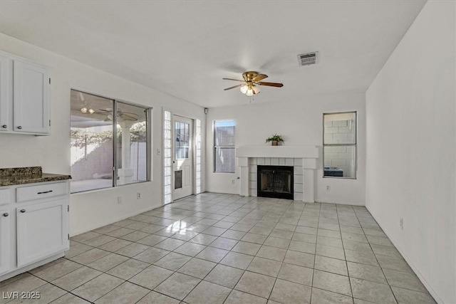 unfurnished living room featuring ceiling fan, a tiled fireplace, and light tile patterned floors