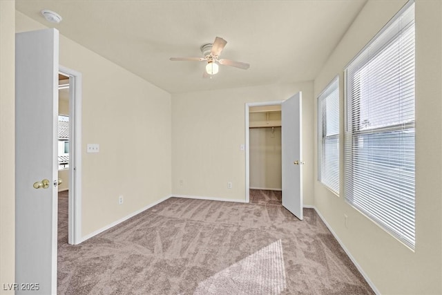 unfurnished bedroom with a walk in closet, light colored carpet, a closet, and ceiling fan