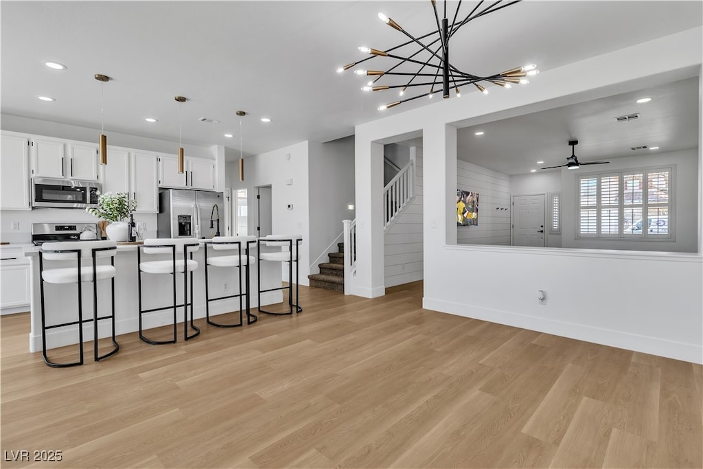 kitchen with stainless steel appliances, decorative light fixtures, a kitchen island with sink, and white cabinets