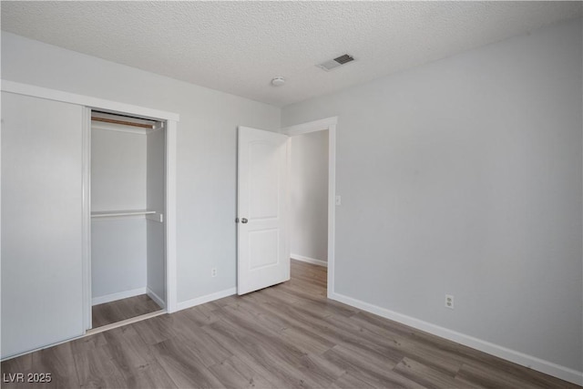 unfurnished bedroom featuring a textured ceiling, light hardwood / wood-style floors, and a closet