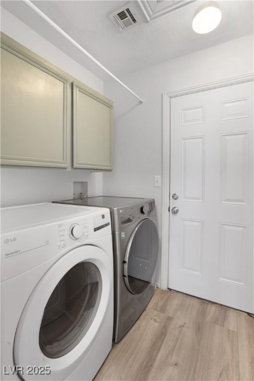 clothes washing area featuring cabinets, washing machine and dryer, and light hardwood / wood-style floors