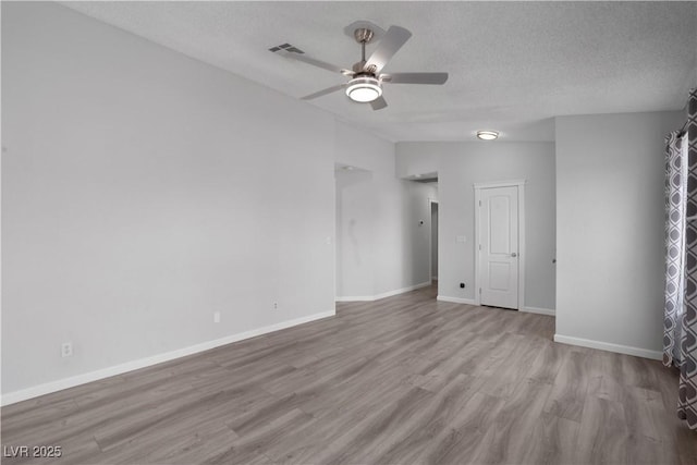 spare room featuring ceiling fan, vaulted ceiling, light hardwood / wood-style flooring, and a textured ceiling