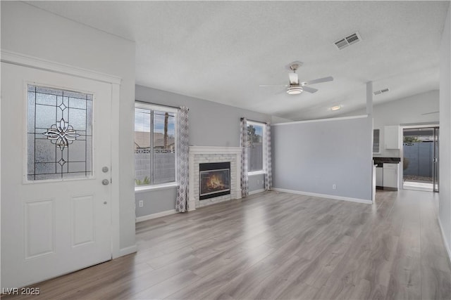 unfurnished living room with ceiling fan, light hardwood / wood-style floors, vaulted ceiling, and a textured ceiling