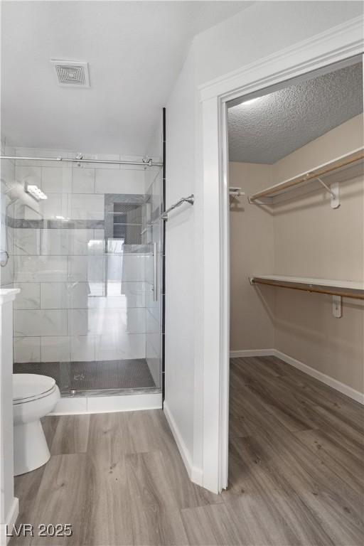 bathroom with hardwood / wood-style flooring, toilet, an enclosed shower, and a textured ceiling