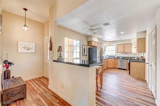 kitchen featuring appliances with stainless steel finishes, pendant lighting, a breakfast bar area, kitchen peninsula, and light wood-type flooring