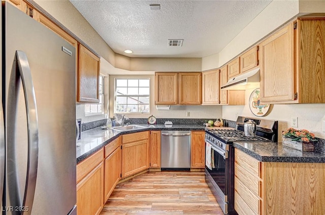 kitchen with sink, a textured ceiling, light brown cabinets, light wood-type flooring, and stainless steel appliances