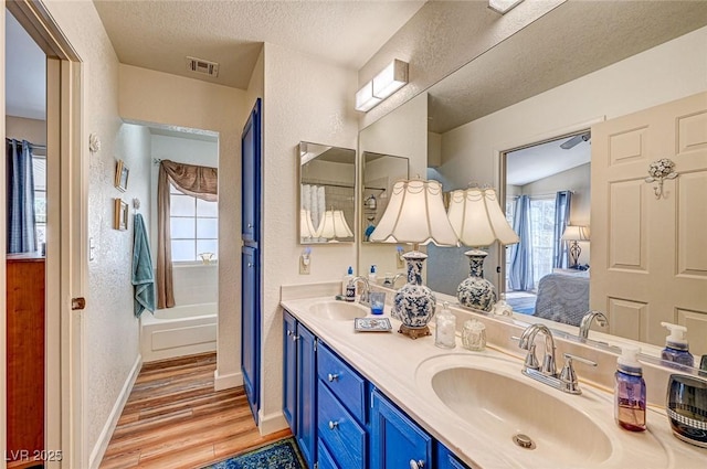 bathroom with hardwood / wood-style flooring, vanity, a textured ceiling, and a tub to relax in