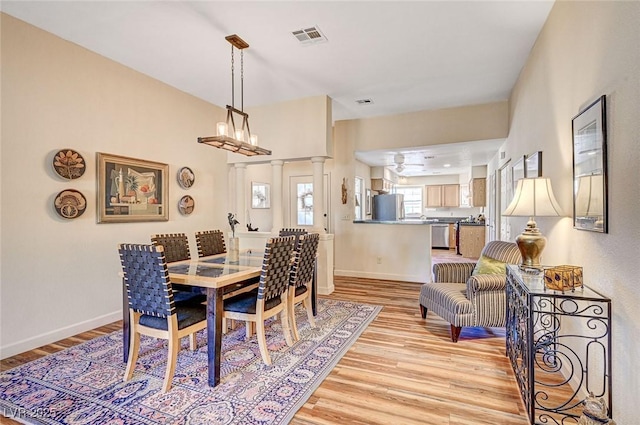 dining room with light hardwood / wood-style floors and ornate columns