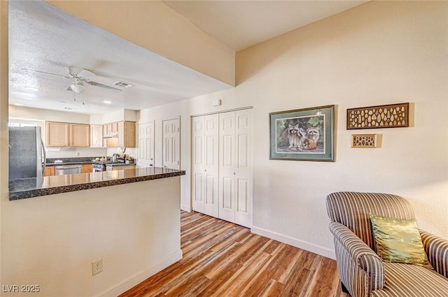 kitchen featuring light brown cabinetry, ceiling fan, kitchen peninsula, stainless steel appliances, and light wood-type flooring