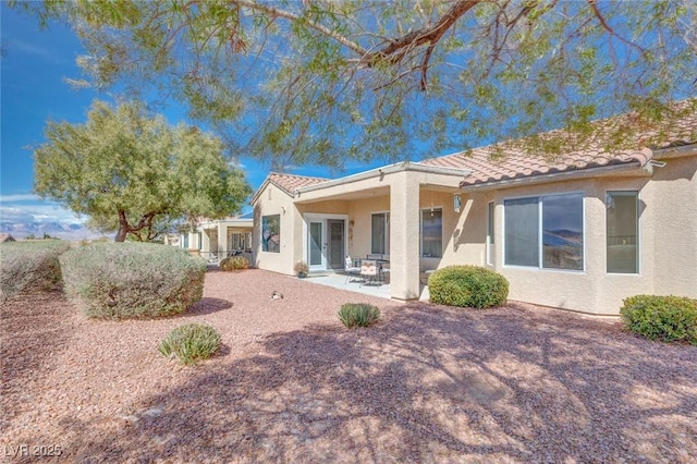 rear view of house with a tile roof, a patio area, and stucco siding