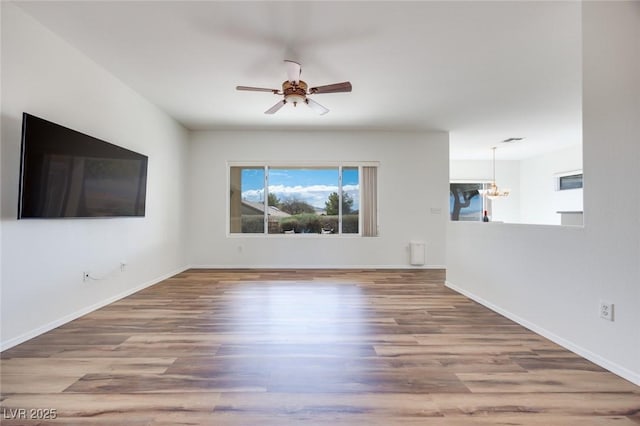 unfurnished living room featuring baseboards, wood finished floors, and ceiling fan with notable chandelier