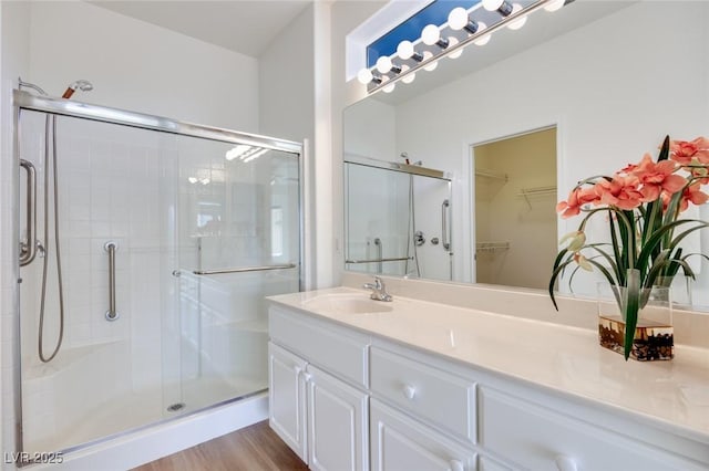 full bath with a stall shower, a spacious closet, vanity, and wood finished floors