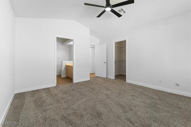 unfurnished bedroom featuring lofted ceiling, a spacious closet, carpet floors, and a textured ceiling