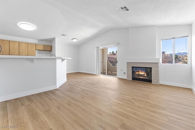 unfurnished living room featuring vaulted ceiling, a tiled fireplace, light hardwood / wood-style floors, and a textured ceiling