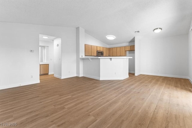 unfurnished living room with lofted ceiling, light hardwood / wood-style flooring, and a textured ceiling