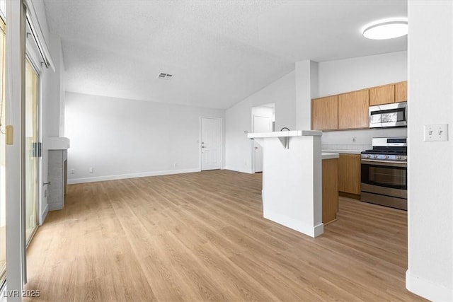 kitchen featuring lofted ceiling, stainless steel appliances, a kitchen bar, and light hardwood / wood-style flooring