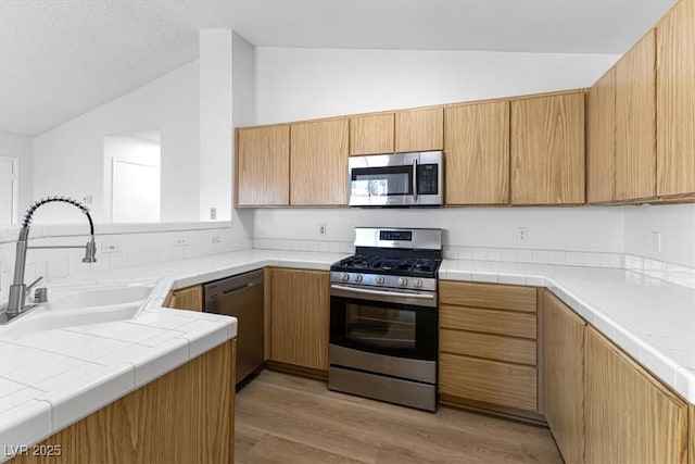 kitchen featuring lofted ceiling, sink, light hardwood / wood-style flooring, appliances with stainless steel finishes, and tile countertops