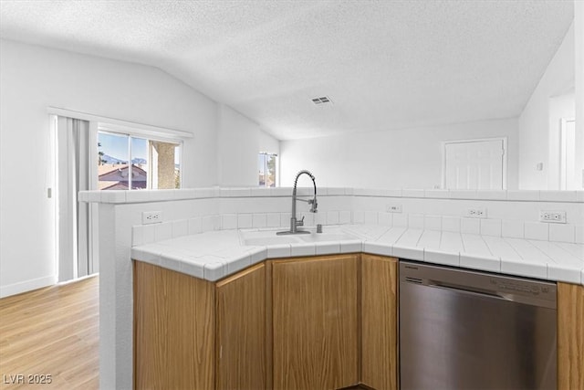 kitchen featuring sink, light hardwood / wood-style flooring, dishwasher, tile counters, and vaulted ceiling