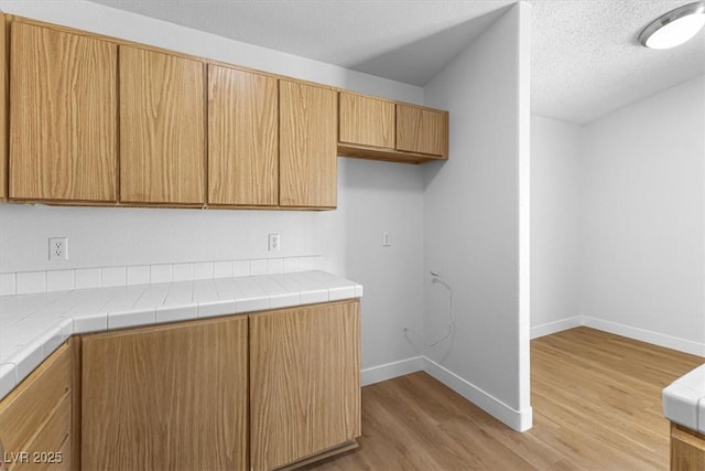 kitchen with tile counters, a textured ceiling, and light wood-type flooring