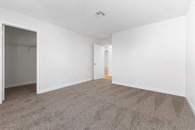 unfurnished bedroom with carpet, a spacious closet, a textured ceiling, and a closet