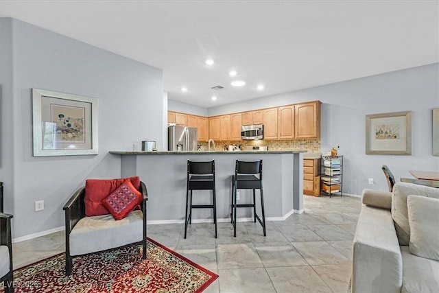 kitchen featuring appliances with stainless steel finishes, a breakfast bar, light brown cabinetry, decorative backsplash, and kitchen peninsula