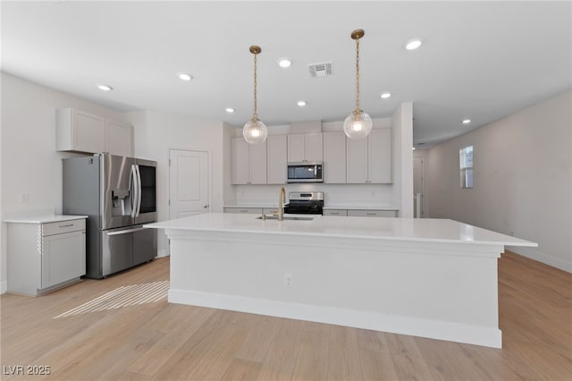 kitchen with sink, hanging light fixtures, appliances with stainless steel finishes, an island with sink, and light hardwood / wood-style floors