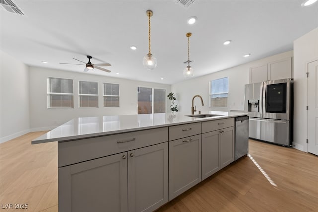 kitchen with sink, gray cabinetry, decorative light fixtures, a center island with sink, and stainless steel appliances