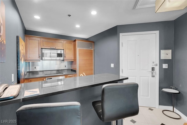 kitchen with brown cabinets, a breakfast bar area, dark countertops, recessed lighting, and appliances with stainless steel finishes