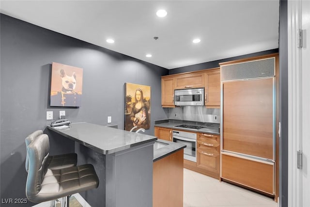 kitchen with a breakfast bar, a peninsula, stainless steel appliances, a sink, and recessed lighting