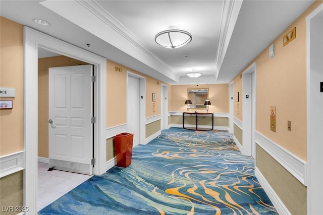 hallway with ornamental molding, tile patterned flooring, a raised ceiling, and baseboards