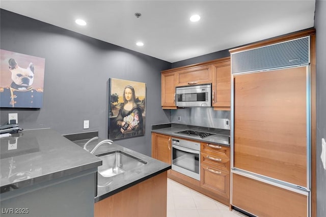 kitchen featuring dark countertops, brown cabinets, stainless steel appliances, a sink, and recessed lighting