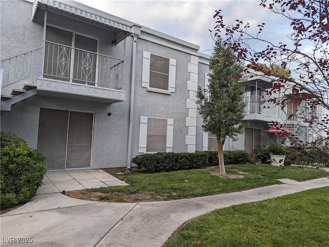 view of front of house featuring a balcony, a front lawn, and stucco siding