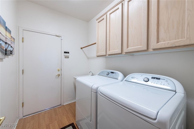 washroom featuring cabinets, washing machine and clothes dryer, and light hardwood / wood-style flooring