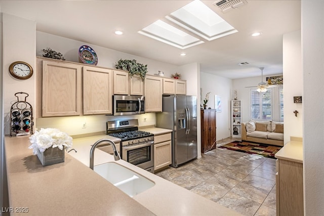 kitchen with light brown cabinetry, a skylight, sink, ceiling fan, and stainless steel appliances