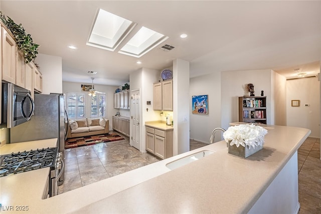 kitchen with appliances with stainless steel finishes, a skylight, sink, and cream cabinetry