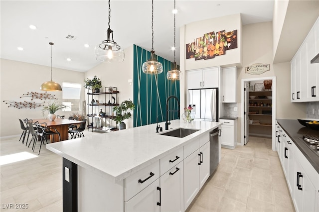 kitchen with sink, hanging light fixtures, stainless steel appliances, an island with sink, and white cabinets