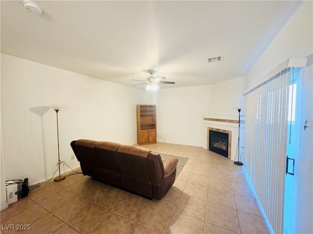 tiled living room with a tile fireplace and ceiling fan