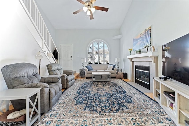 living room with a tile fireplace, a towering ceiling, and ceiling fan