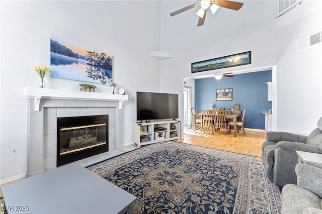 living room featuring a tiled fireplace, hardwood / wood-style floors, ceiling fan, and a high ceiling