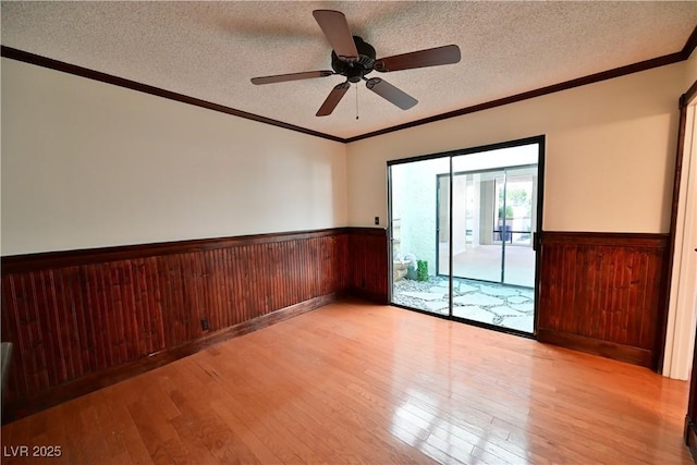 unfurnished room featuring crown molding, wood walls, a textured ceiling, and light hardwood / wood-style flooring